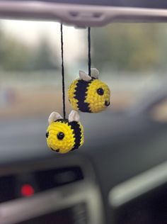 two yellow and black crocheted bees hanging from a car dash board or dashboard