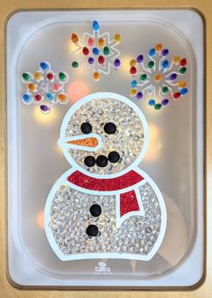 a snowman made out of plastic beads on a white tray with lights behind it