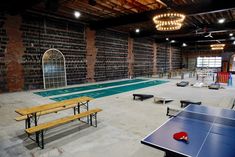 an indoor ping pong table and benches in a large room with brick walls on the ceiling