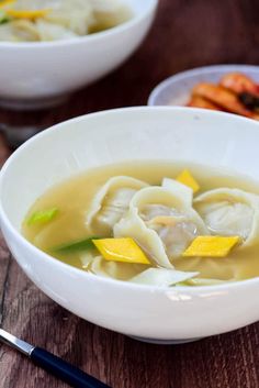 two bowls filled with dumplings and carrots on top of a wooden table next to chopsticks