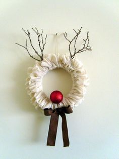 a wreath with branches and a red ornament hanging from the front on a wall