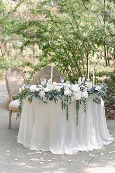 a table with white flowers and greenery is set up for an outdoor wedding reception