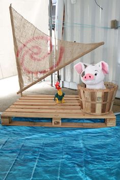 a wooden boat with a pig on it and a toy sailboat in the background