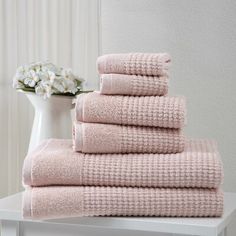 a stack of pink towels sitting on top of a white table next to a vase with flowers