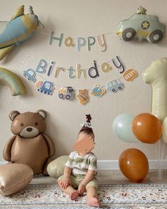 a baby is sitting on the floor in front of balloons and decorations for a birthday