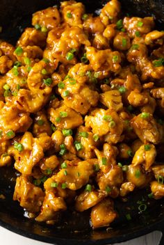 chicken with sauce and green onions in a black skillet on a white counter top