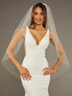 a woman wearing a white wedding dress with a veil on her head and hands on her hips