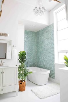 a white bath tub sitting next to a green plant in a bathroom under a window