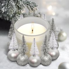 a white candle surrounded by silver ornaments and christmas tree decorations on a snow - covered surface