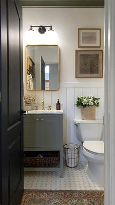 a white toilet sitting next to a sink in a bathroom under a mirror and framed pictures on the wall