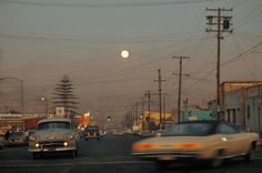 cars are driving down the street in front of power lines and telephone poles at dusk