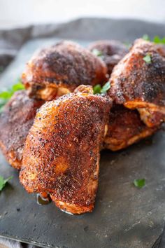 three pieces of chicken on a slate board with parsley sprinkled over them