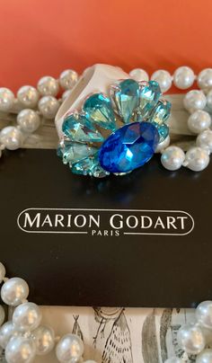 MARION GODART Paris Bague Fleur Bleu Strass taille 59 eu Spectacular statement rhinestone flower ring handmade by Marion Godart. It features a large blue faceted prong set rhinestone surrounded by 10 drop-shaped light blue rhinestones creating a mid-century style flower ring. The whole sits on a hard as glass white resin base-ring. This impressive ring measures a little over 1 3/4 inch diameter and 5/8 inch high, US ring size 9. This ring is unique, completely designed and handmade by Marion God Paris Bracelet, French Jewelry, Scarf Rings, Bold Rings, French Designer, Rhinestone Ring, Rhinestone Flower, Cat Brooch, Blue Rhinestones