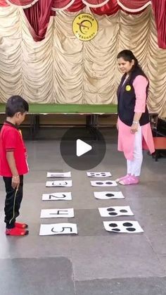 two children are standing in front of some cut out numbers on the floor with red curtains behind them