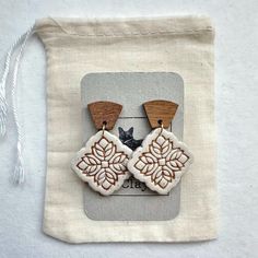 two wooden earrings with white and brown designs on them, sitting in front of a bag