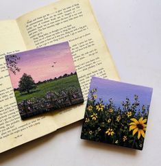 an open book with two pictures of flowers on the pages and a photo of a field in the background