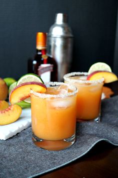 two glasses filled with drinks sitting on top of a table next to sliced peaches