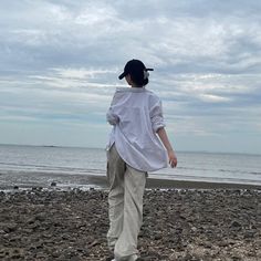 a woman standing on top of a rocky beach next to the ocean under a cloudy sky