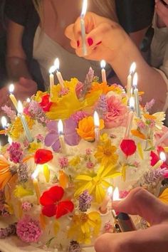 a woman lighting candles on a birthday cake with flowers and daisies in front of her