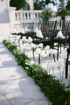 rows of black chairs with white flowers on the side and greenery in between them