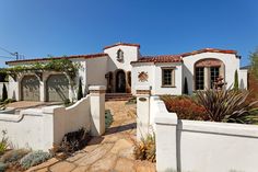 a white stucco house with red tile roofing and door, surrounded by greenery