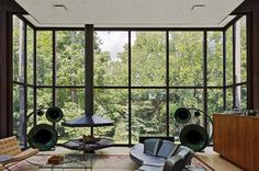 a living room with large windows and furniture in front of the window is a tree filled forest