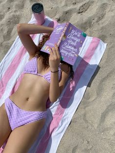 a woman laying on top of a pink and white towel next to a purple book