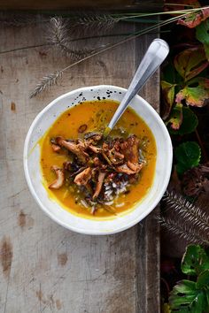 a white bowl filled with soup next to green plants and leaves on a wooden table