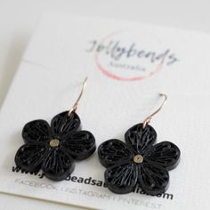 two black flower shaped earrings on top of a white piece of paper next to a card