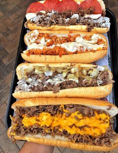 four sandwiches in buns with meat, cheese and onions on them sitting on a tray