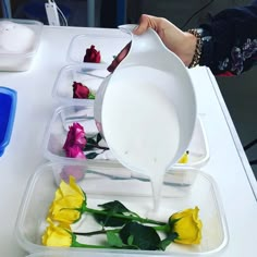 a person pouring water into a container filled with yellow and pink roses on a table