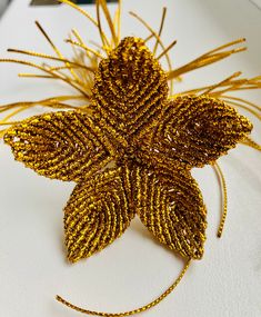 a close up of a flower made out of gold thread and beads on a white surface