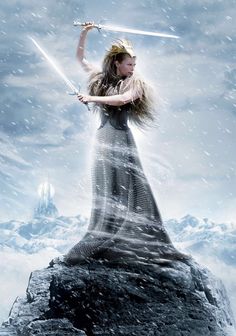 a woman holding two swords standing on top of a rock in the middle of snow