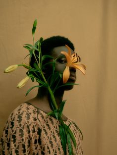 a woman with flowers on her face and hair in front of her face, against a beige background