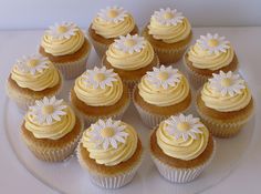 twelve cupcakes with yellow frosting and daisies on top are arranged in a circle