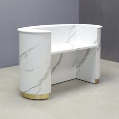 a white marble desk with gold accents on the top and bottom, in front of a gray wall