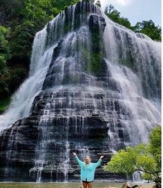 a woman standing in front of a waterfall with her arms spread out and hands up