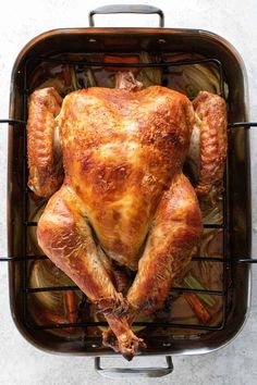 a roasted turkey in a roasting pan with onions and carrots