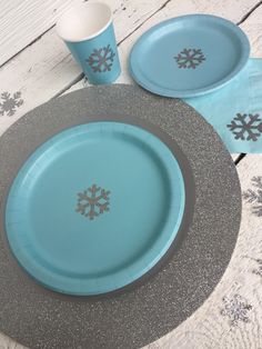 a table set with plates, cups and napkins for snowflake themed party