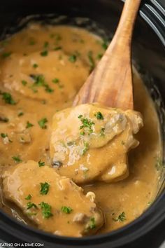 a wooden spoon in a slow cooker filled with chicken and gravy, garnished with parsley