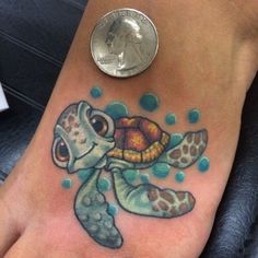 a small foot tattoo with a sea turtle on it's side and a penny sitting next to it