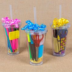 four plastic cups with different colored straws and pens in them on a brown surface