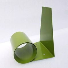 a green metal object sitting on top of a white table next to a black cup