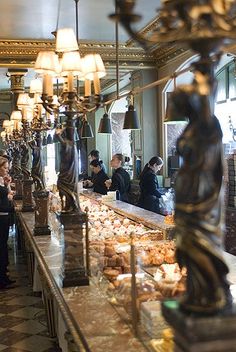 people are standing at the counter in a fancy restaurant with chandeliers hanging from the ceiling