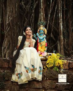 a woman sitting on top of a stone wall next to a statue in the woods