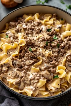 a bowl full of pasta with meat and mushrooms in sauce on the side, next to an eggplant sprig