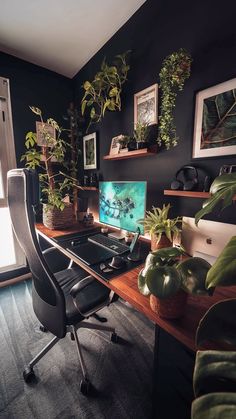 a desk with a computer, plants and pictures on the wall