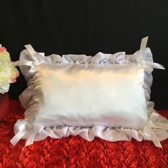 a white pillow with ruffles on it and a flower in a vase next to it