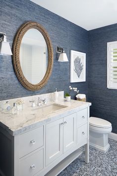 a bathroom with blue walls and white fixtures, including a round mirror above the sink