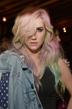 a woman with pink, green and yellow hair wearing a jean jacket at a party